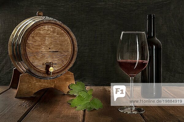 Ein Glas Rotwein mit einer Flasche  einem Weinfass und Weinblättern  Seitenansicht auf einem dunklen rustikalen Hintergrund  Low Key Foto mit einem Platz für Text