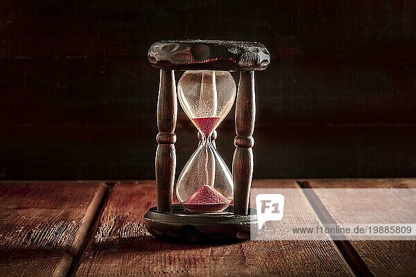 Zeit Konzept. Eine Sanduhr mit Sand fallen durch  auf einem dunklen rustikalen hölzernen Hintergrund mit einem Platz für Text