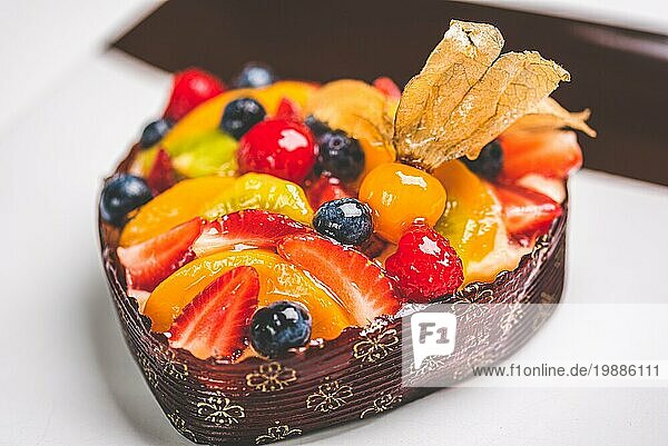 Herzförmige Fruchtbiskuit  Obsttorte auf einem quadratischen Teller auf dem Tisch. Gesunde Süßwaren Hintergrund. Platz für Text