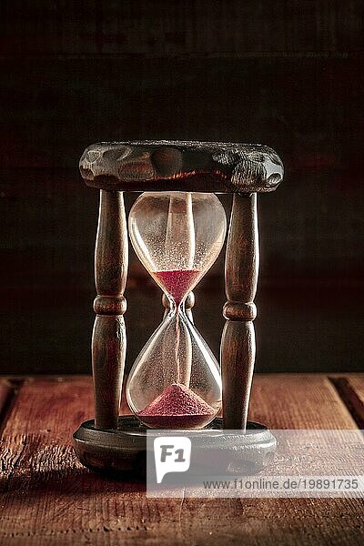 Die Zeit läuft aus Konzept. Ein Stundenglas mit Sand fallen durch  auf einem dunklen rustikalen Hintergrund