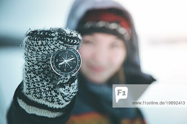 Junge lächelnde Frau hält einen Kompass hoch. Winterzeit  Handschuhe und Kapuze