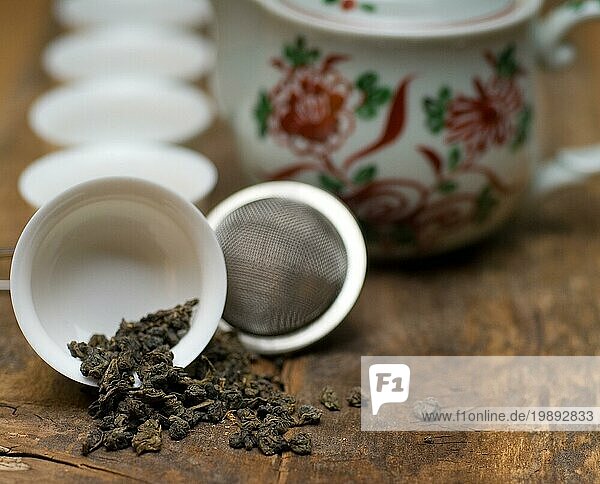 Trockenes grünes chinesisches Teeset mit Sieb in Großaufnahme  Tassen und Teekanne im Hintergrund auf altem Holzbrett  Food photography