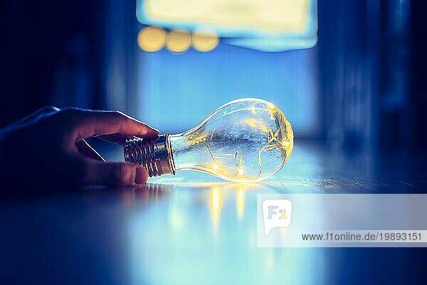 Die Hände halten eine LEDglühbirne über dem Holzboden. Symbol für Ideen und Innovation. Fenster und Licht im unscharfen Hintergrund