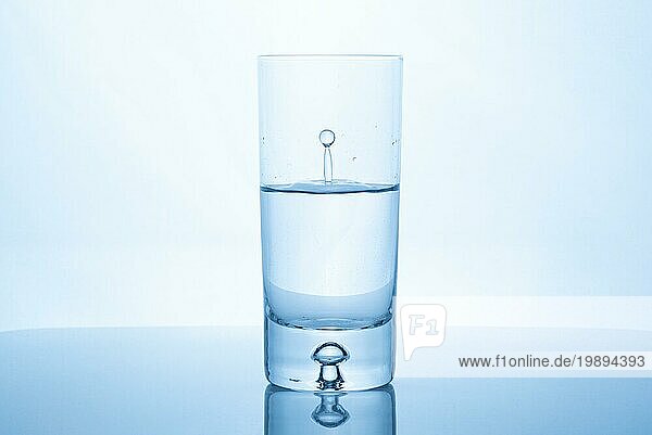 Wassertropfen spritzen in Glas halb voll gegen hellen Hintergrund. Reinheit und Gesundheit Konzept
