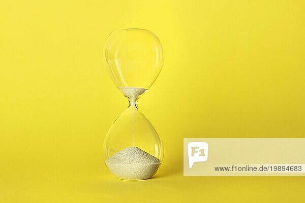 Die Zeit läuft aus Konzept. Eine Sanduhr mit Sand fallen durch  auf einem leuchtend gelben Hintergrund mit Kopie Raum