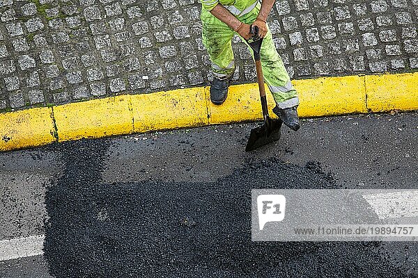 Arbeiter mit einer Schaufel macht eine Pause bei der Reparatur einer Straße mit Asphalt auf einer Stadtstraße. Hohe Winkelansicht