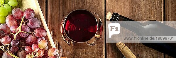 Weinverkostung Panorama. Ein Rotweinglas mit einer Flasche  Trauben und einem alten Korkenzieher  aufgenommen von oben auf einem dunklen rustikalen Holzhintergrund
