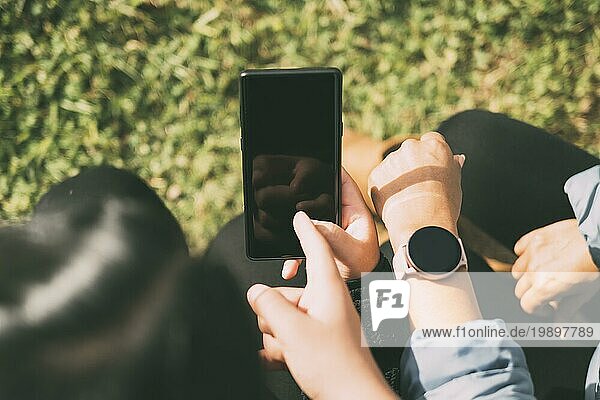 Blick auf die Hand  die den Bildschirm eines Smartphones und einer Smartwatch berührt  drei Personen  die Informationen über soziale Medien auf intelligenten mobilen Geräten austauschen  natürlicher grüner Hintergrund  unscharf
