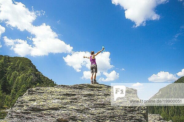 Ziel erreicht: Sportliches Mädchen steht auf einem großen Felsen und hebt die Hände in die Luft
