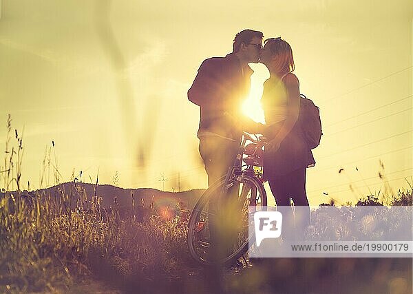 Junges Paar mit Fahrrad küsst sich auf einem Feld  Sonnenuntergang