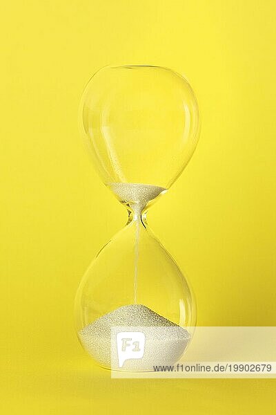 Die Zeit läuft ab Konzept. Ein Stundenglas mit Sand tropft durch  auf einem leuchtend gelben Hintergrund