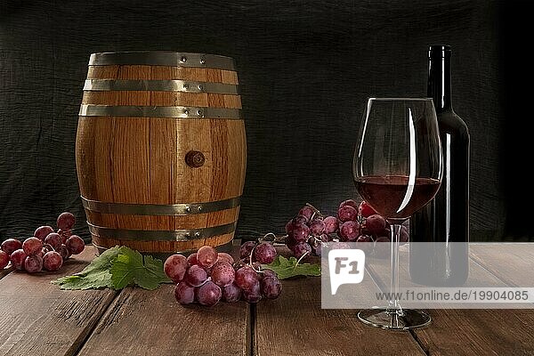 Ein Glas Rotwein mit einer Flasche  ein Weinfass  Trauben und Weinblätter  auf einem dunklen rustikalen Hintergrund  Low Key Foto mit Kopie Raum