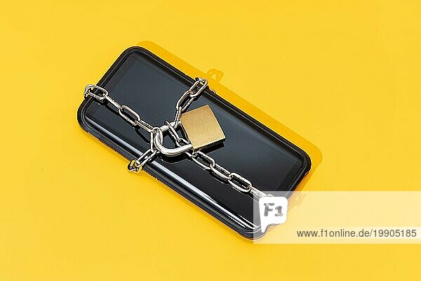 Telefon Sicherheitskonzept. Smartphone mit Kette und Vorhängeschloss auf gelbem Hintergrund gesperrt. Mobile Sicherheit und Datenschutz