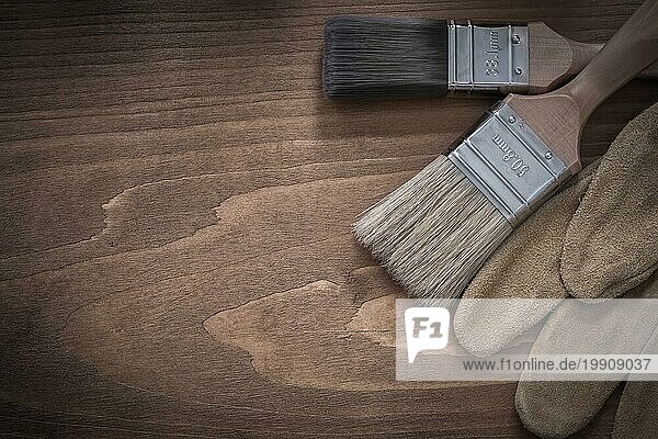 Pinsel und braune Schutzhandschuhe aus Leder auf einer Holzfläche
