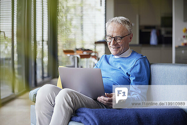 Senior man sitting on couch at home using tablet PC