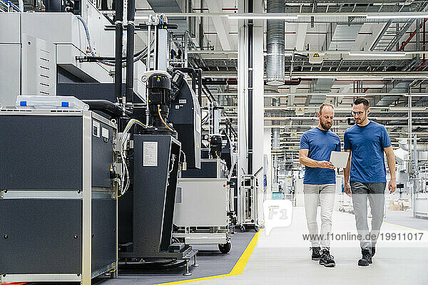 Two colleagues with digital tablet walking in a factory