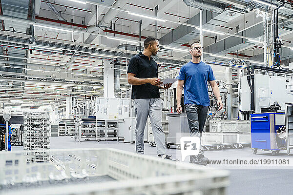 Two colleagues with digital tablet walking in a factory