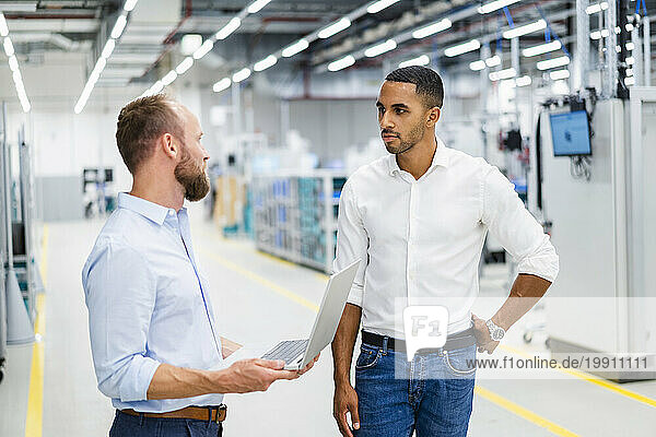 Two businessmen with laptop having a meeting in a factory