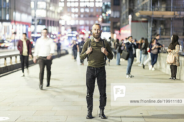 Mature man with backpack standing on footpath in city
