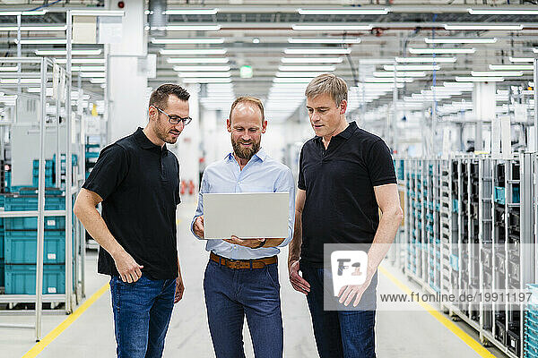 Businessman sharing laptop with employees in a factory