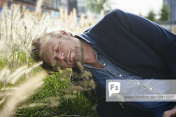 Mature businessman with eyes closed leaning on grass