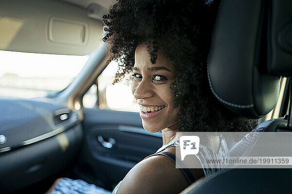 Happy woman looking over shoulder sitting in car