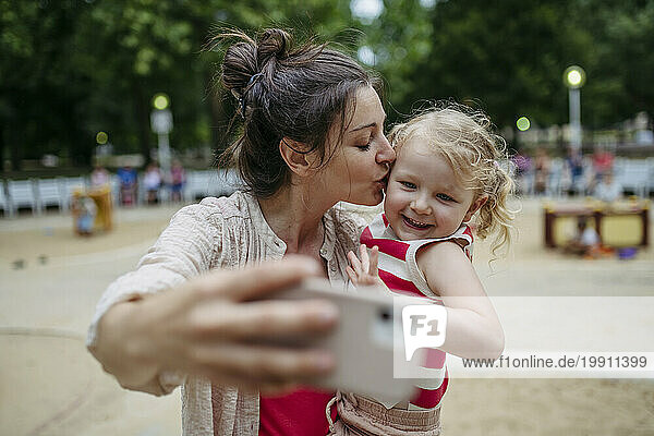 Little toddler girl and mother having fun at playground taking selfies with smartphone