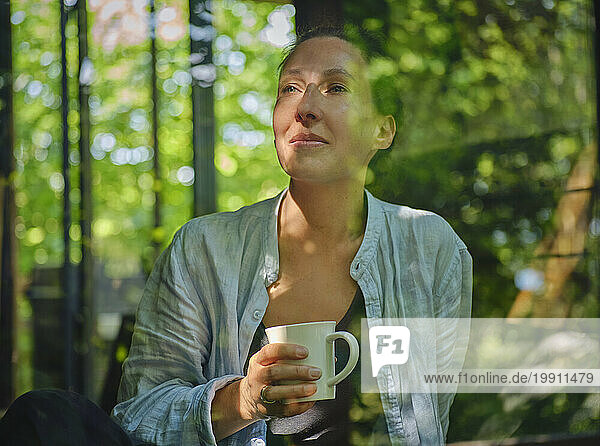 Woman with cup in hand looking through window