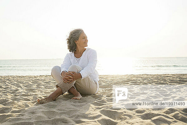 Smiling mature woman sitting on sand at beach