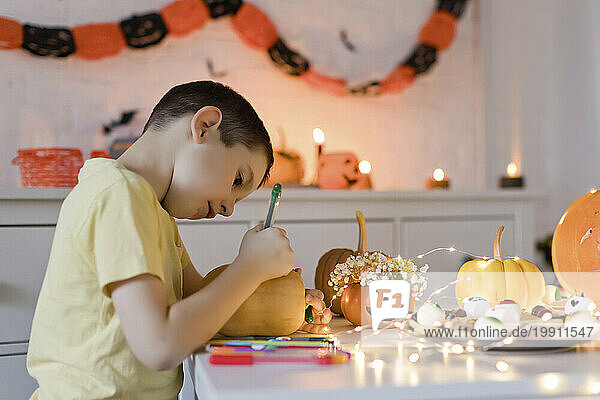 Boy drawing on pumpkin with colored pen at home