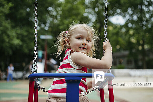 Smiling girl sitting in swing at gthe playground
