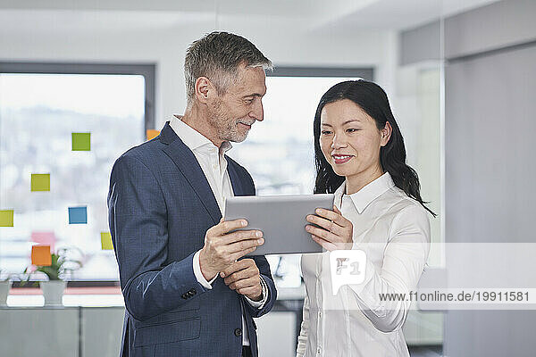 Smiling businesswoman having discussion over tablet PC with colleague in office