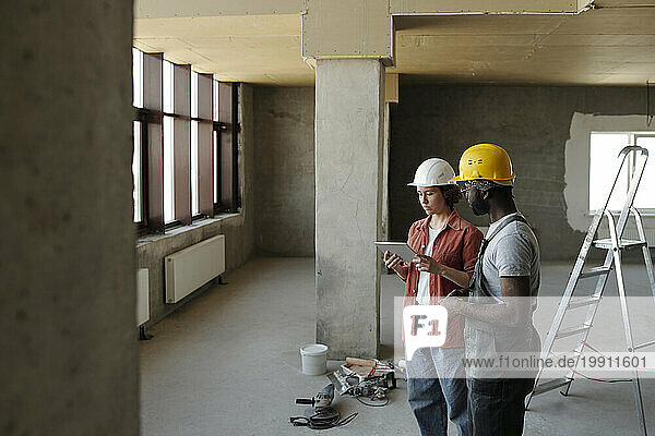 Engineer using tablet PC and planning with coworker at construction site