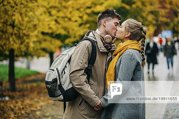 Romantic woman kissing boyfriend with backpack at street