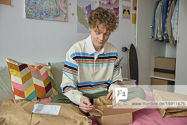 Blond man unpacking box on bed in bedroom at home