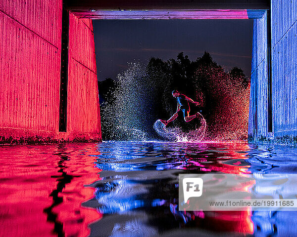 Man jumping in river water under bridge with neon lights at night