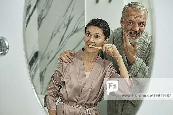 Man cuddling his wife brushing teeth in front of mirror