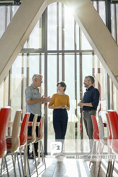 Senior businessman explaining to colleagues near glass window in office