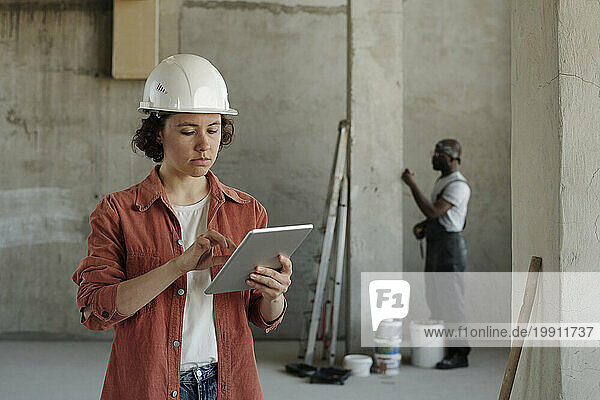 Young engineer using tablet PC with coworker in background at construction site
