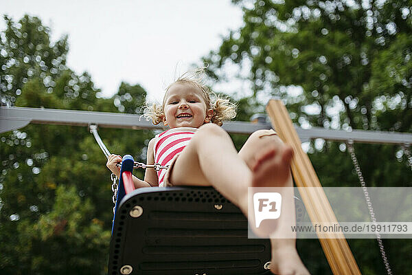 Little toddler girl and mother have fun at playground swinging on a swing