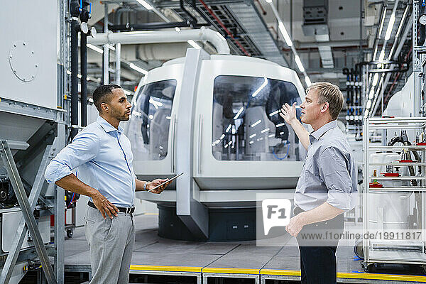 Two businessmen having a meeting at modern machine in a factory