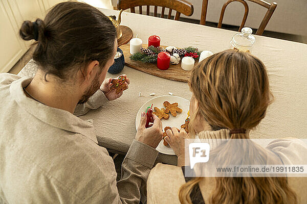 Couple decorating cookies at table in kitchen