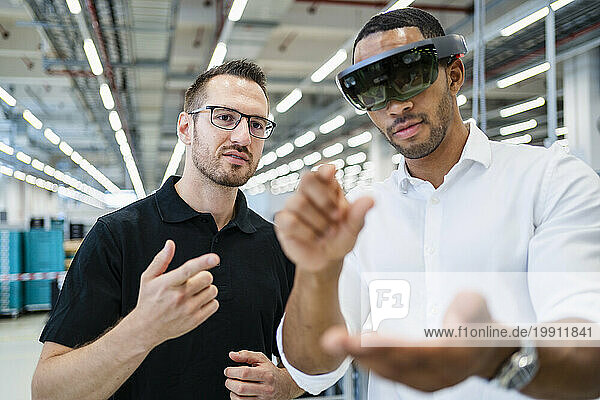 Technician wearing augmented reality glasses in a factory interacting with colleague