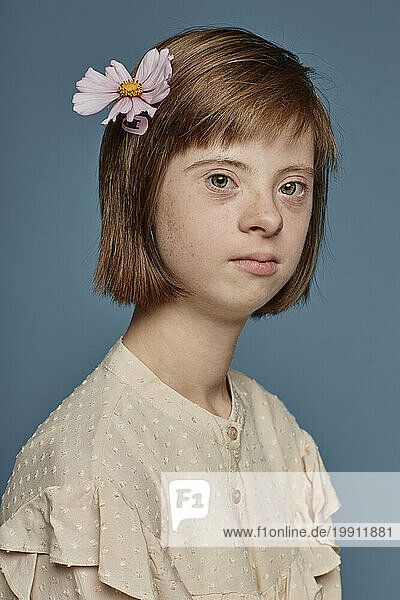 Teenage girl with Down syndrome with flower in hair by blue background