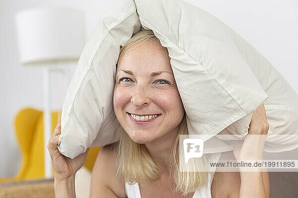 Smiling woman holding pillow overhead at home