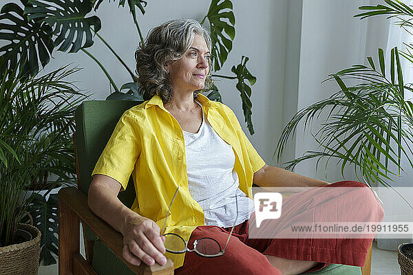 Mature woman day dreaming sitting cross-legged on armchair at home
