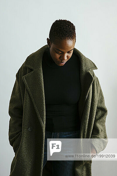 Woman looking down wearing long coat against white background