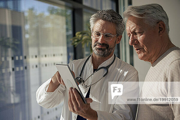 Senior doctor discussing with man over tablet PC in hospital