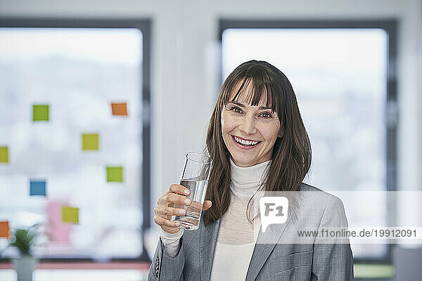 Happy mature businesswoman holding glass of water in office