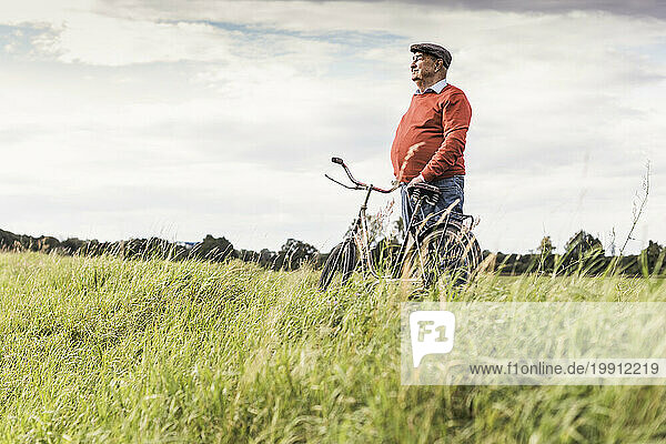 Senior man standing by bicycle and looking at view in field